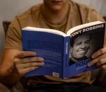 Close-up of a person reading 'Poder Sem Limites' by Tony Robbins indoors.